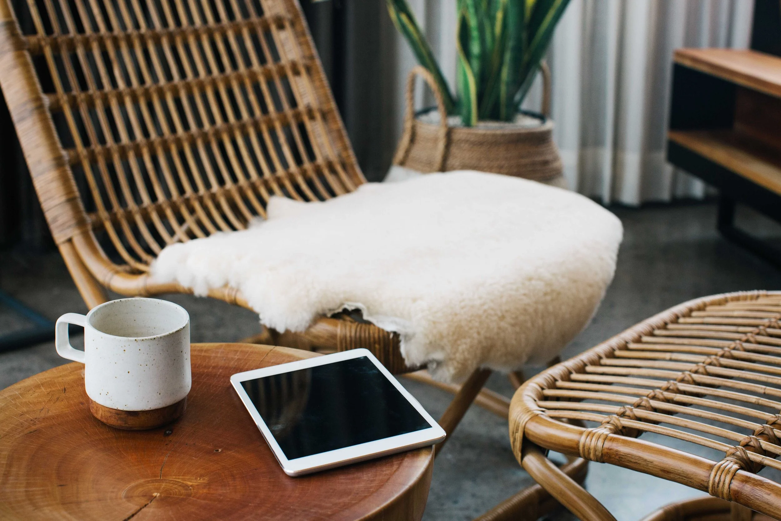 A tablet and mug on a table beside a warm woven chair.